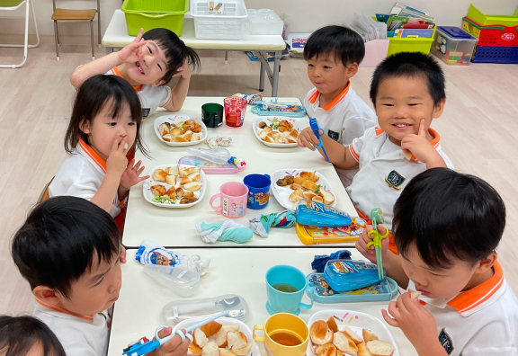  子どもたちが食事を囲んで座っている様子。笑顔で楽しそうに会話しながら、食事を楽しんでいます。